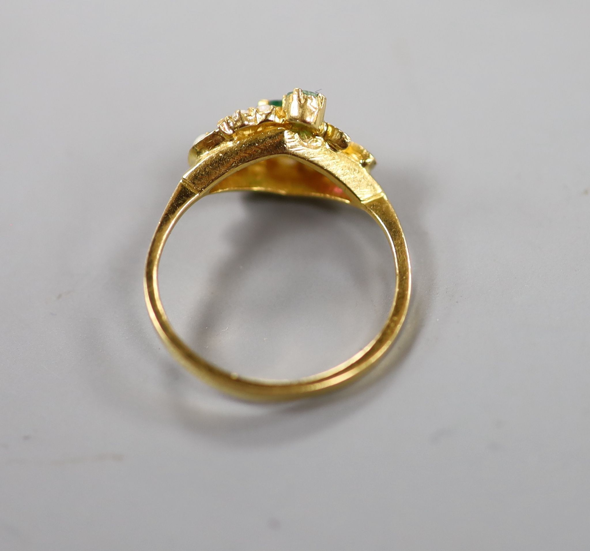A modern yellow metal, emerald, ruby and seed pearl cluster set crossover ring, size L, gross weight 2.9 grams.